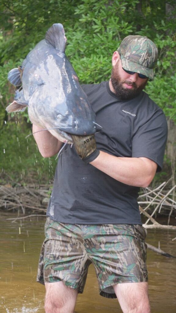 Man holding catfish in water werting shorts