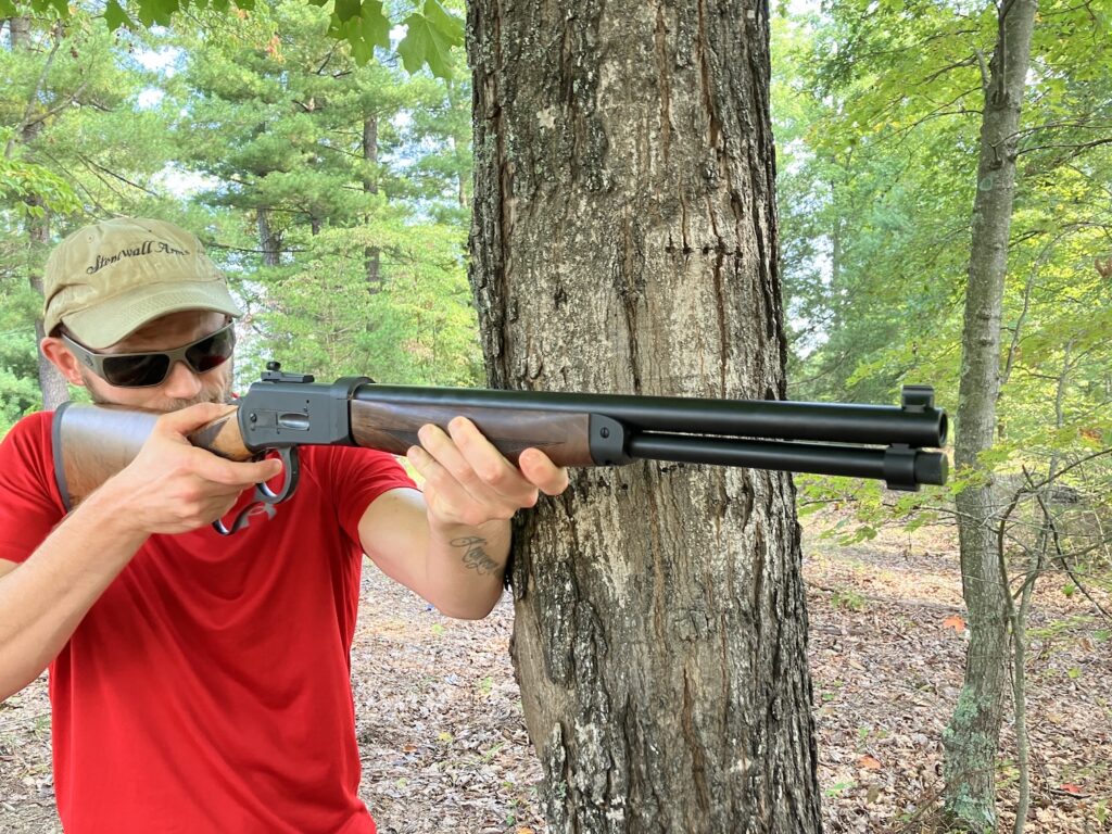 man supporting rifle on side of tree